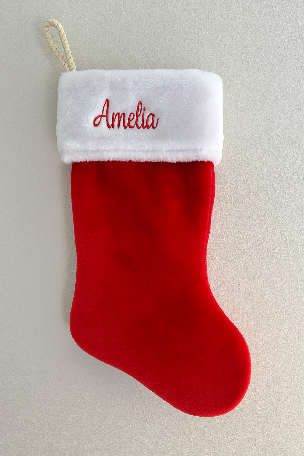 Red Christmas stocking with white cuff embroidered with 'Amelia' on a light gray background