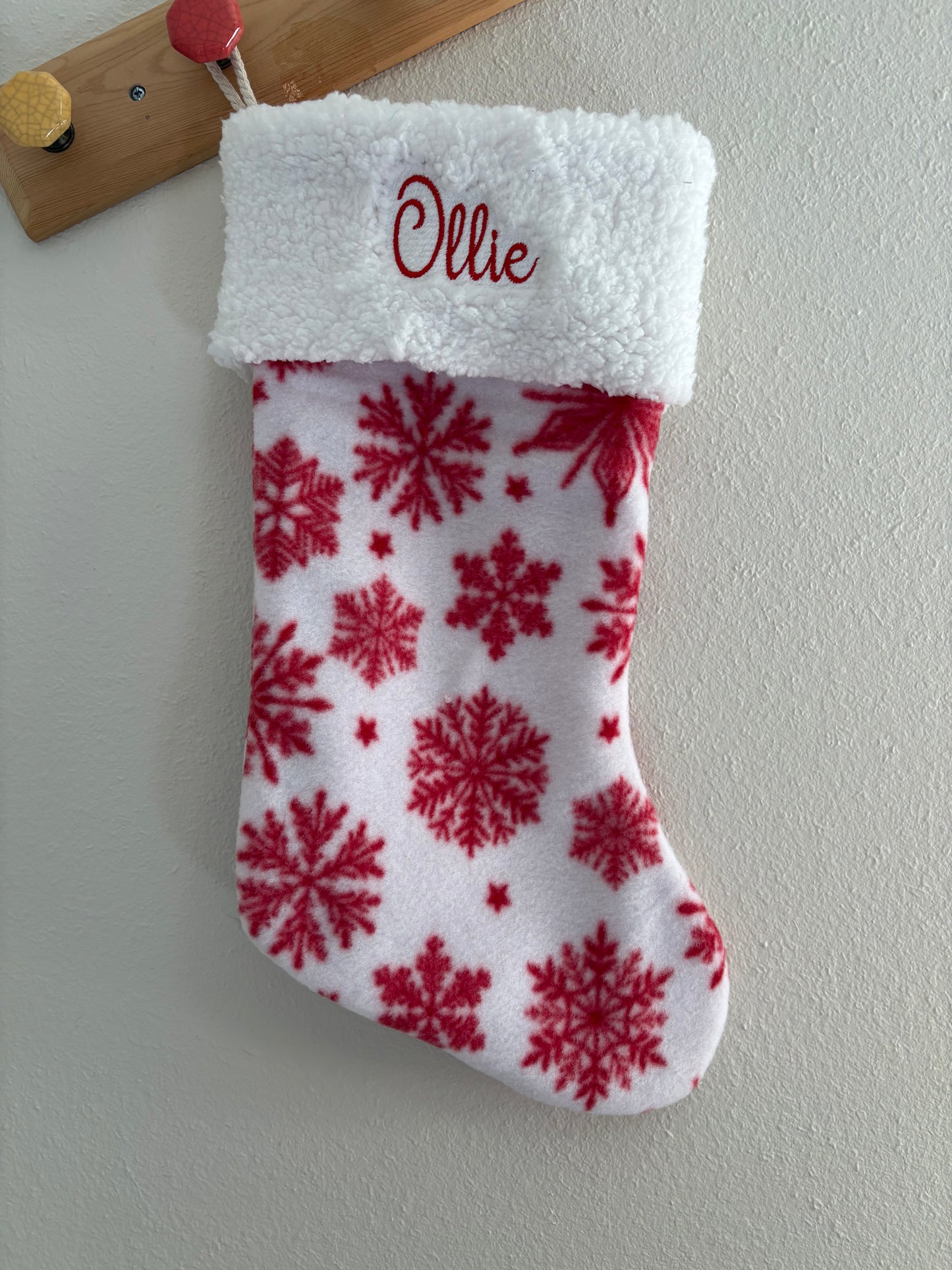 White Christmas stocking with red snowflake pattern and 'Olivia' embroidery, hanging on a white wall.
