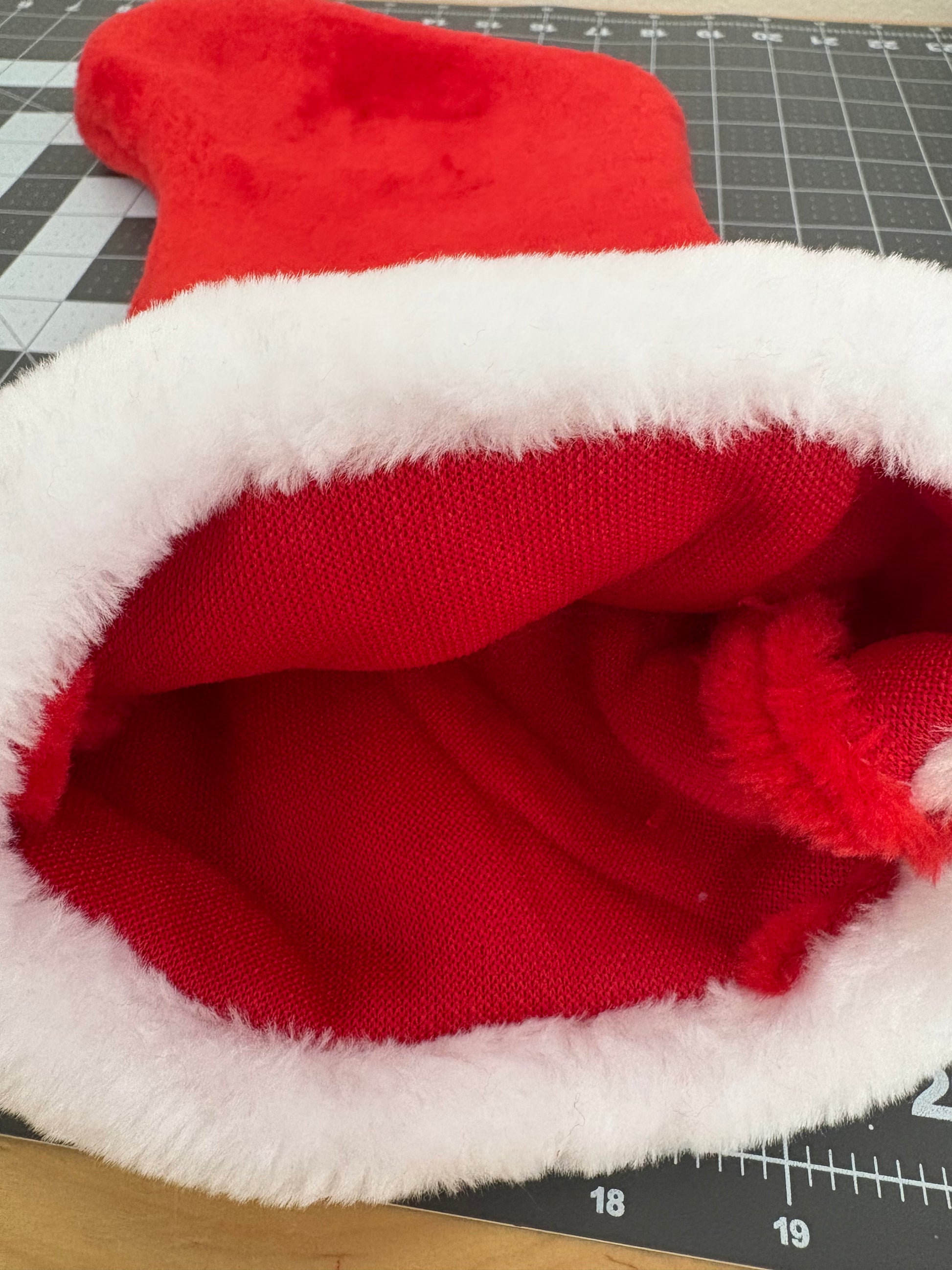 Close-up of a red and white plush toy on a cutting mat with a ruler.